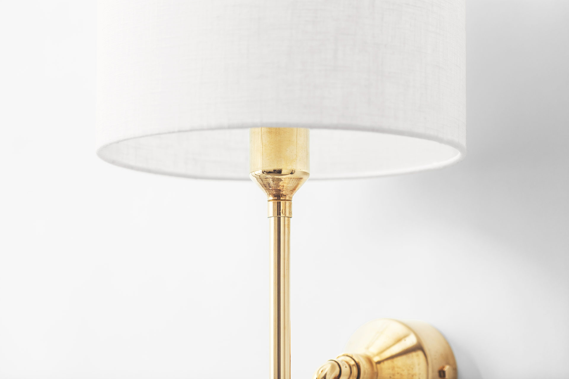 Contemporary bedside sconce in brass with white linen shade