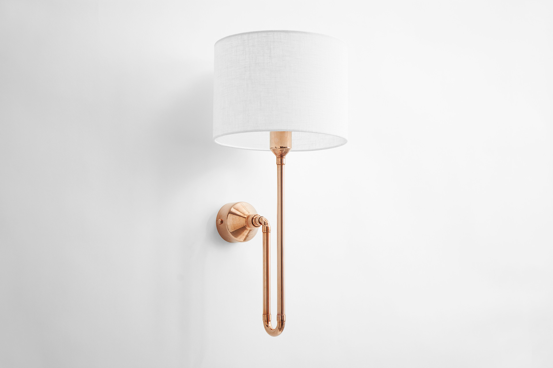 Designer conceptual wall lamp in pink copper metal finish with natural white linen shade in urban loft bedroom